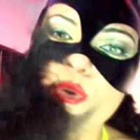 Woman plays with her boobs and rides a dildo in red body harness and black latex mask